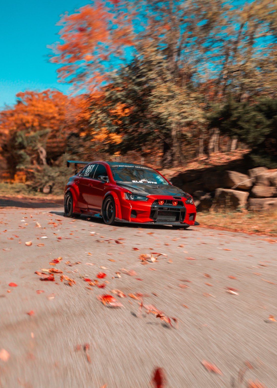 Red Mitsubishi Lancer Evolution in motion on a winding autumn road
