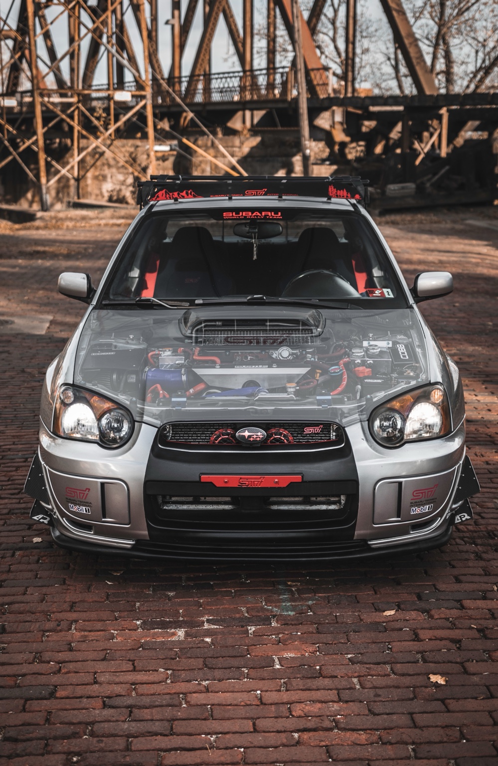 Modified silver Subaru WRX STI photographed beneath an industrial bridge